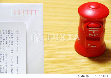 木目のテーブルに置いた郵便ポスト形の貯金箱と礼文の封筒 86267101