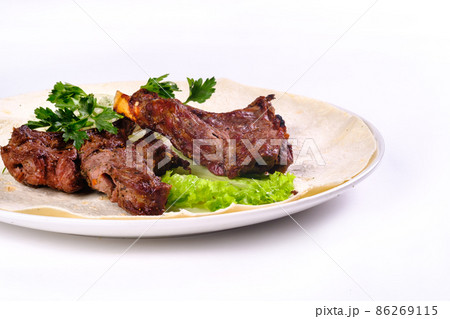 Meat kebab on ribs on lavash with onions and cabbage on a white plate, on an isolated white background Meat kebab on ribs on lavash with onions and cabbage on a white plate, on an isolated white background 86269115