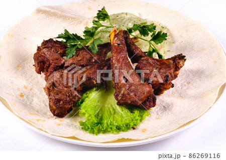 Meat kebab on ribs on lavash with onions and cabbage on a white plate, on an isolated white background 86269116