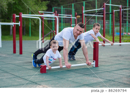Caucasian man goes in for sports on the sports ground with his sons. Caucasian man goes in for sports on the sports ground with his sons. 86269794