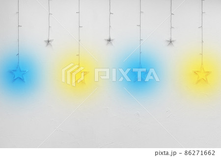 Colored bright garlands in the form of stars on a white empty wall of the interior background decor Colored bright garlands in the form of stars on a white empty wall of the interior background decor 86271662