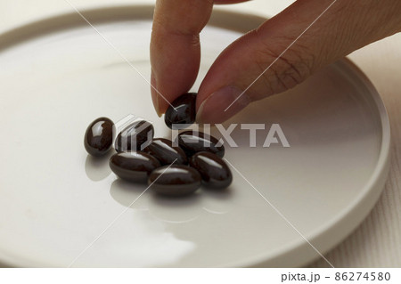 白い皿の上の黒色のサプリメントの粒 86274580