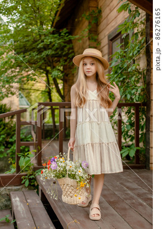 Carefree tween girl with basket of wildflowers standing on doorstep of country house Carefree tween girl with basket of wildflowers standing on doorstep of country house 86276165