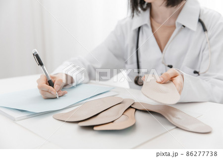 Doctor holding an insole while sitting at a table. Orthopedist tests the medical device. Orthopedic insoles. Foot care. Flat Feet Correction. Treatment and prevention of flat feet and foot diseases. 86277738