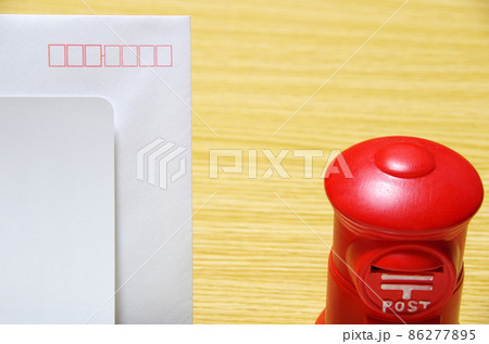 木目のテーブルに置いた郵便ポスト形の貯金箱と礼状の封筒（コピースペース有り） 86277895