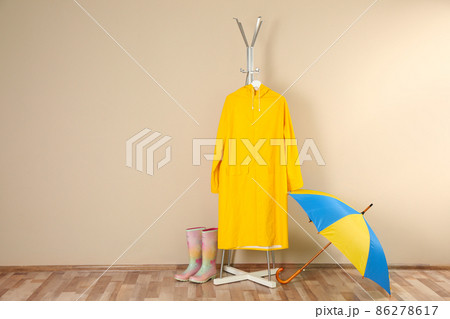 Umbrella, rain coat and rubber boots near beige wall. Space for text 86278617
