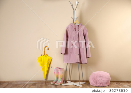 Yellow umbrella, raincoat and rubber boots near beige wall 86278650