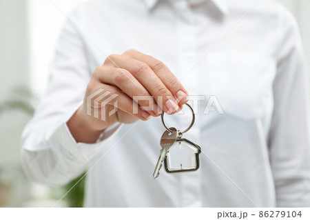Real estate agent holding house key with trinket indoors, closeup 86279104