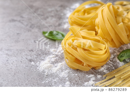 Uncooked tagliatelle pasta on grey table, closeup. Space for text 86279289