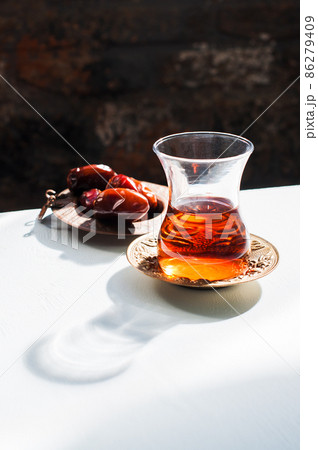 Red tea in glass, dates in the plate and hard light with harsh shadows, Close up. 86279409