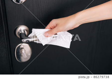 Cleaning black door handles with an antiseptic wet wipe. Woman hand using towel for cleaning home room door link. Sanitize surfaces prevention in hospital and public spaces against corona virus. Cleaning black door handles with an antiseptic wet wipe. Woman hand using towel for cleaning home room door link. Sanitize surfaces prevention in hospital and public spaces against corona virus. 86279738