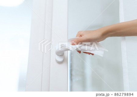 Cleaning door handles with an antiseptic wet wipe and gloves. Woman hand using towel for cleaning home room door link. Sanitize surfaces prevention in hospital and public spaces against corona virus. 86279894