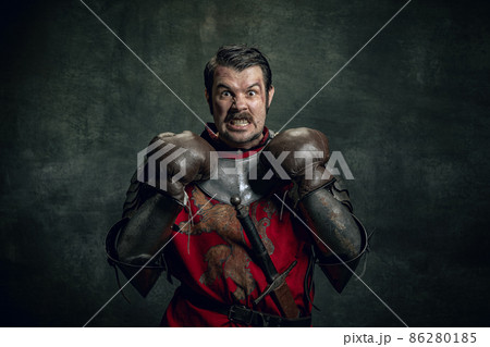 Portrait of medieval warrior or knight with dirty wounded face in boxing gloves isolated over dark background. Comparison of eras, history Portrait of medieval warrior or knight with dirty wounded face in boxing gloves isolated over dark background. Comparison of eras, history 86280185