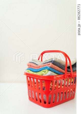 Multi-colored towels lie in a red laundry basket on a white background. Laundry and ironing. Multi-colored towels lie in a red laundry basket on a white background. Laundry and ironing. 86282771