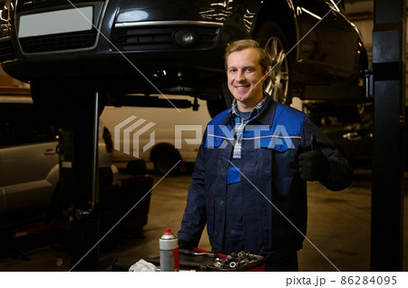 Professional portrait of a handsome Caucasian man, auto mechanic, technician, car engineer, smiling at camera standing near a box with set of tools for repairing automobiles in the repair shop garage 86284095