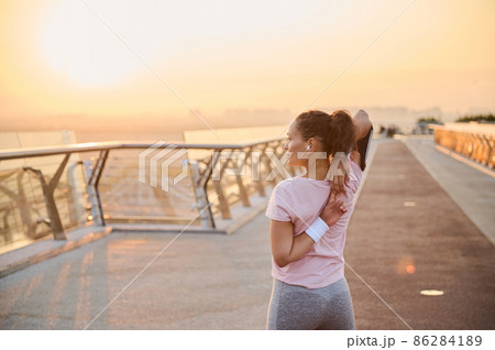 Rear view of a determined female athlete, sportswoman stretching her arms, raising them up, exercising at sunrise. Fitness, health, body care, sport and active lifestyle concept 86284189