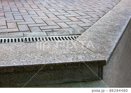 Pavement drainage grate with line iron grill on rectangular stone tile walkway on edge of cliff, close-up of drainage system on dry weather, nobody. 86284480
