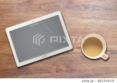 原油価格の推移が映るタブレット端末とコーヒーカップ 86293619