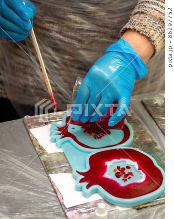 The art process of pouring epoxy resin into a wooden toy. Technology process of creating a painting in style resin art, works with epoxy in studio, makes a wooden stand with the image. Close up. The art process of pouring epoxy resin into a wooden toy. Technology process of creating a painting in style resin art, works with epoxy in studio, makes a wooden stand with the image. Close up. 86297752