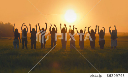 Silhouette of friends of 11 girls waving their hands at sunset in the field. Silhouette of friends of 11 girls waving their hands at sunset in the field. 86299763