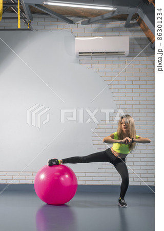 Sports girl in leggings and top posing with sports equipment. Fitness woman performs exercise with fitness ball 86301234