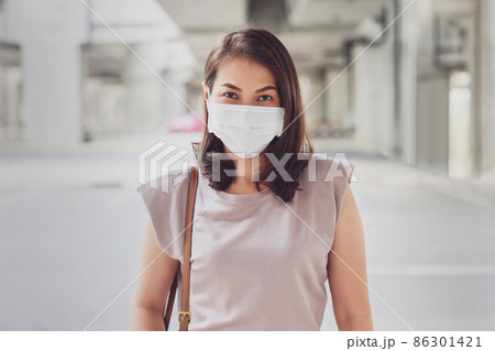 Asian woman wearing protective face mask standing and looking at camera outside in an urban construction background with copy space. Concept of new normal lifestyle and prevents the COVID-19 virus 86301421