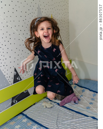 A little girl is jumping and playing in her room on the bed and laughing. 86307557