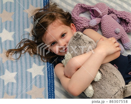 A little girl hugs her soft toys on the bed in her room. A little girl hugs her soft toys on the bed in her room. 86307558