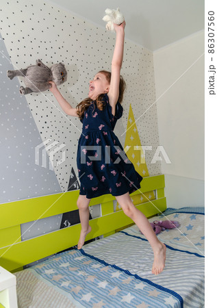 A little girl is jumping and playing in her room on the bed and laughing. A little girl is jumping and playing in her room on the bed and laughing. 86307560