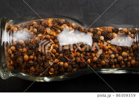 A mixture of seasonings, spices and herbs in a glass mill on a black background. A mixture of seasonings, spices and herbs in a glass mill on a black background. 86309359