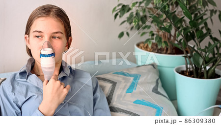 Teenage girl makes inhalation with a nebulizer equipment. Sick child holding inhalator in hand and breathes through an inhaler at home 86309380