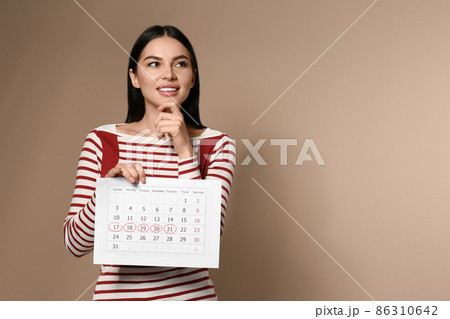 Pensive young woman holding calendar with marked menstrual cycle days on beige background Pensive young woman holding calendar with marked menstrual cycle days on beige background 86310642