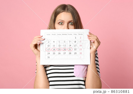 Excited young woman holding calendar with marked menstrual cycle days on beige background 86310881
