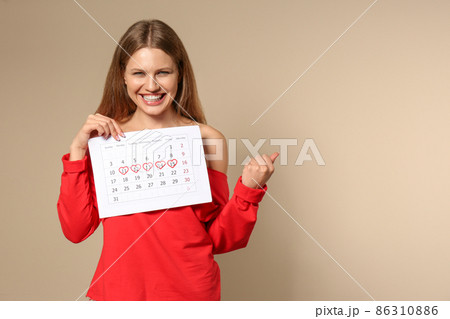 Excited young woman holding calendar with marked menstrual cycle days on beige background Excited young woman holding calendar with marked menstrual cycle days on beige background 86310886