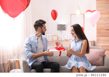 Happy young couple with heart shaped balloons and gift box isolated on white Happy young couple with heart shaped balloons and gift box isolated on white 86311280