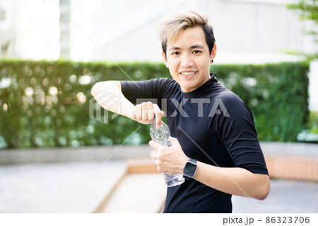 Active Asian sportsman relaxing and drinking a water in bottle after outdoor running or workout. Asian man drink a water during the break from exercise. A healthy man trying hard for cardio workout. Active Asian sportsman relaxing and drinking a water in bottle after outdoor running or workout. Asian man drink a water during the break from exercise. A healthy man trying hard for cardio workout. 86323706