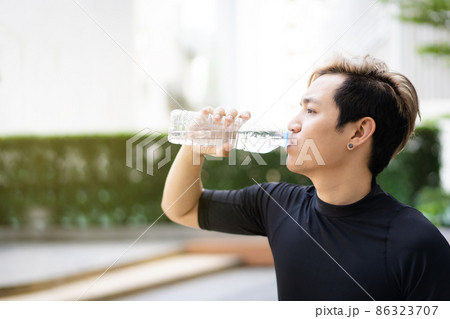 Active Asian sportsman relaxing and drinking a water in bottle after outdoor running or workout. Asian man drink a water during the break from exercise. A healthy man trying hard for cardio workout. 86323707