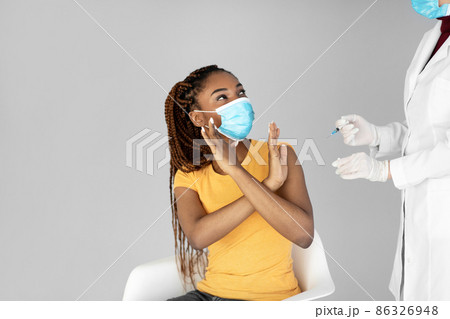 Young black woman in medical face mask stopping doctor from making covid vaccine shot on grey studio background Young black woman in medical face mask stopping doctor from making covid vaccine shot on grey studio background 86326948
