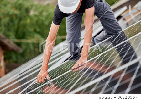 Man technician mounting photovoltaic solar moduls on roof of house. Cropped view of builder in helmet installing solar panel system with help of hex key. Concept of alternative, renewable energy. 86328567