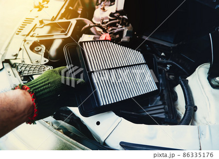A mechanic is replacing an air filter in the engine car filter socket, automotive part concept 86335176