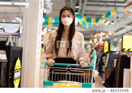 Beautiful attractive asian woman wearing medical face mask and rubber gloves for protected virus and bacteria smile with shopping cart in supermarket happiness and enjoy,Shopping in Grocery Concept 86335446