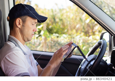 Focused deliveryman checking mobile phone in car Focused deliveryman checking mobile phone in car 86340421