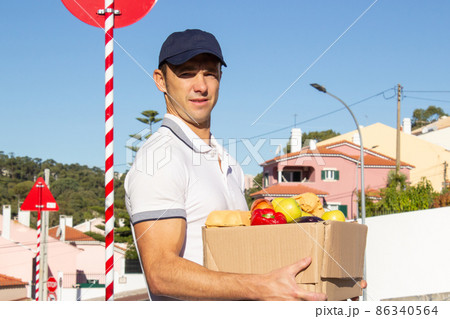 Portrait of mid adult deliveryman carrying box with products Portrait of mid adult deliveryman carrying box with products 86340564