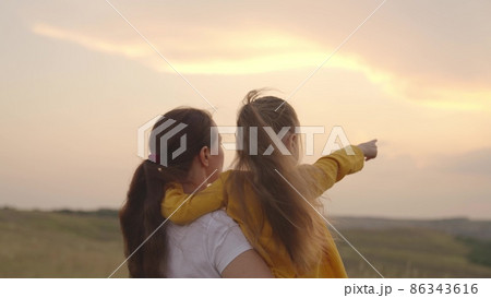 child with mother hugging at sunset, children shows mom by hand at sunset, childhood dream, happy family, love to travel together with family, kid and parent in nature sun, little daughter mom arms 86343616