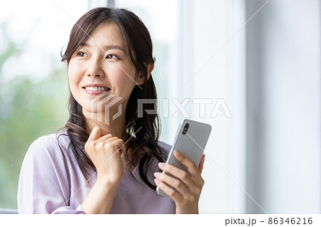 部屋の中でスマホを操作している笑顔の女性 86346216