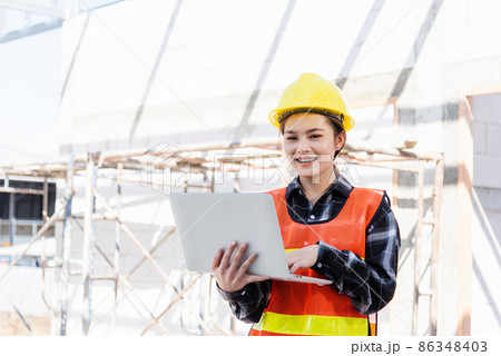 Asian engineer architect worker woman holding laptop inspect and oversee infrastructure progress at construction site 86348403