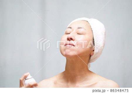 頭にタオルを巻いて首・顔にミストをかける素顔の中年女性　 86348475