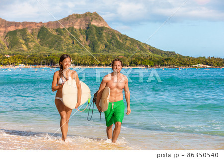 Hawaii surfers couple surf people having fun surfing on Waikiki beach, Honolulu, Oahu island, Hawaii. Asian woman, caucasian man interracial group of friends running out of ocean carrying surfboards 86350540