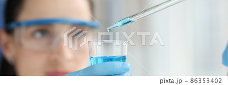 Female scientist dripping and pipetting into flask of blue liquid 86353402