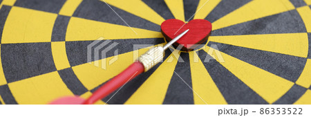 Red small wooden heart in center of dart board and dart closeup 86353522